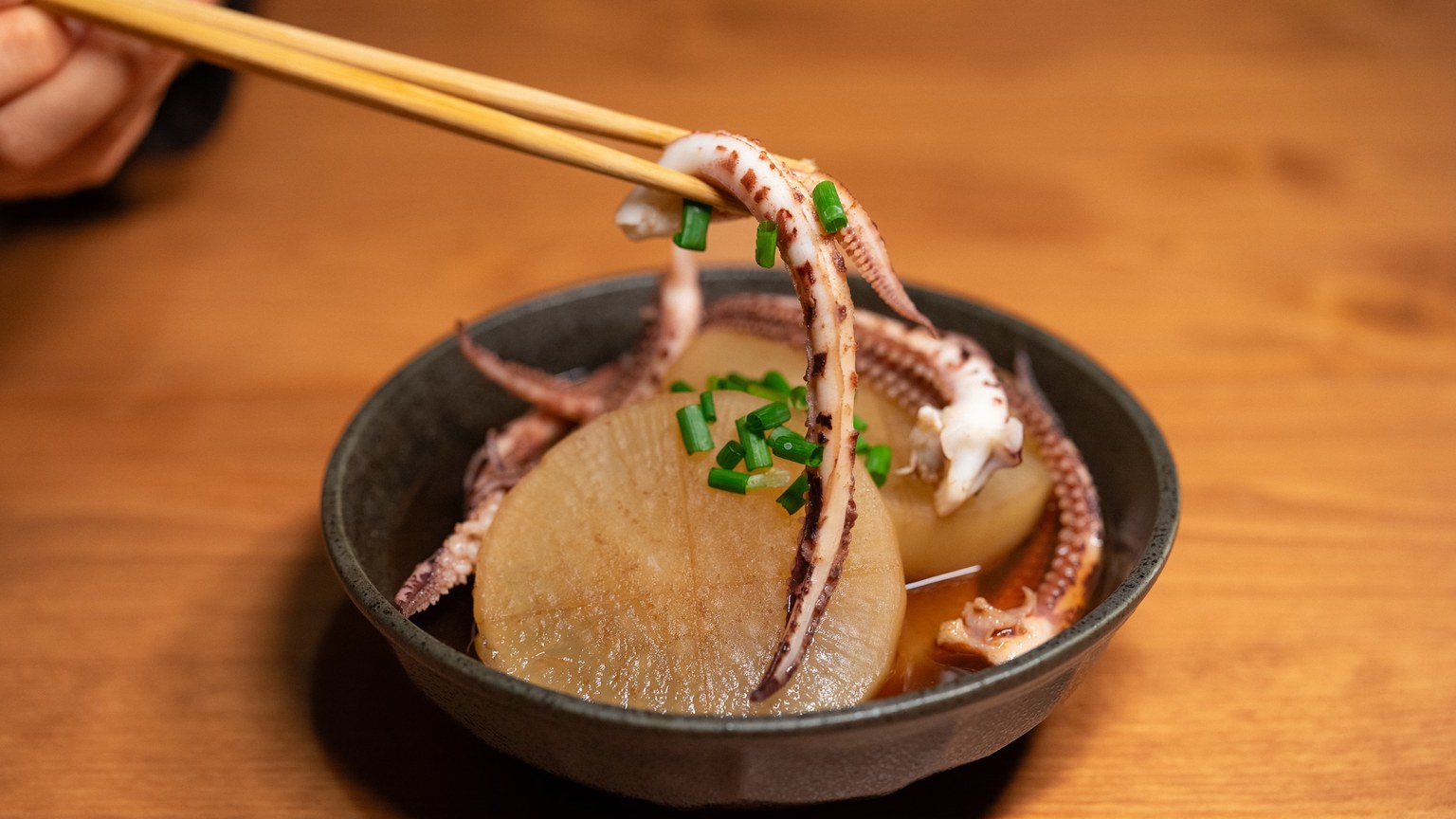 Japanese squid and daikon dish garnished with spring onions in a black bowl.