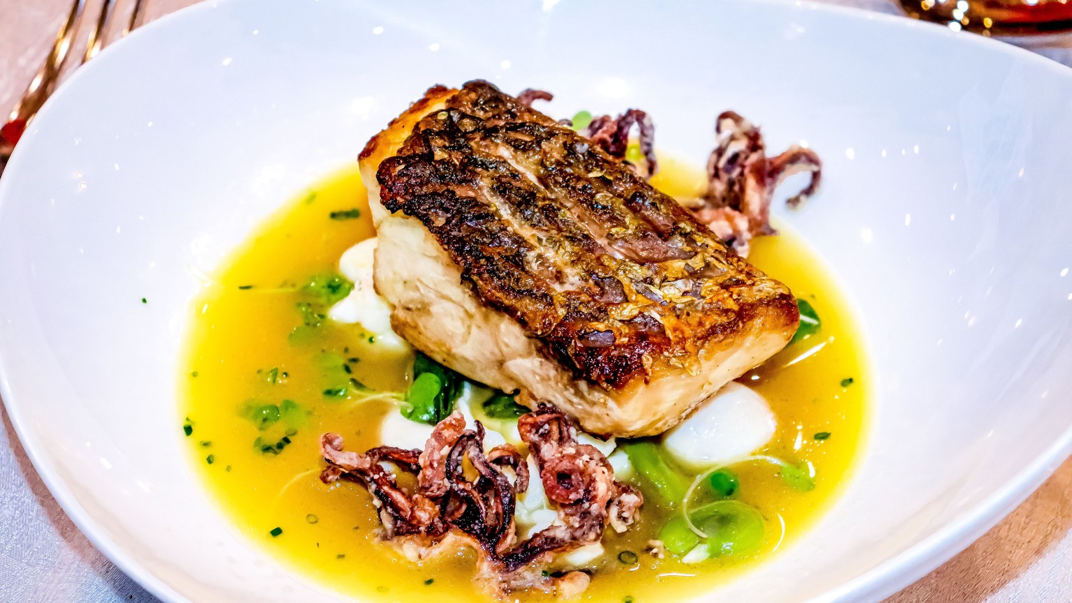 A gourmet dish featuring seared fish with squid, served in a yellow sauce with peas.
