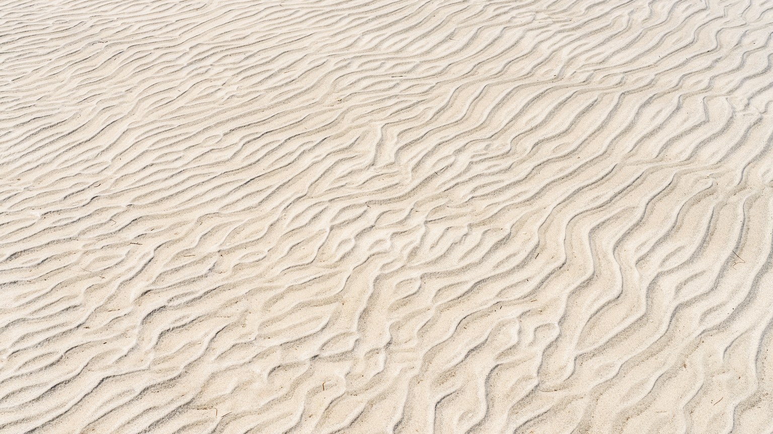 Close-up of rippled sand patterns illuminated by the sun, showcasing natural textures and beach vibes.