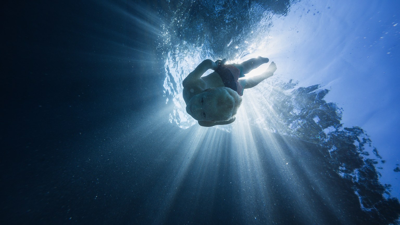 Child diving underwater with sun rays filtering through, creating a magical aquatic scene.
