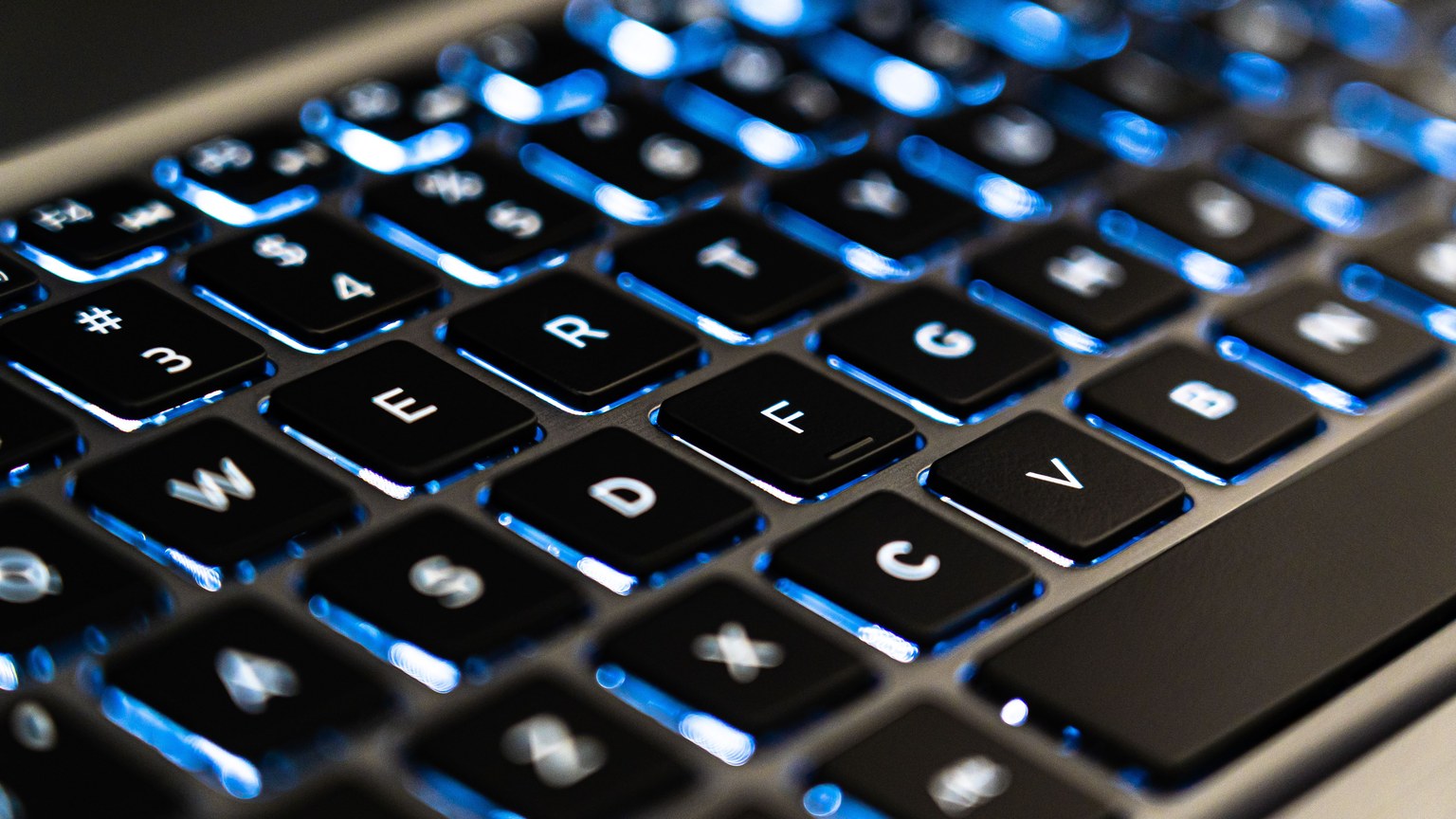 Detailed view of a backlit laptop keyboard keys with blue LED lighting for tech concepts.