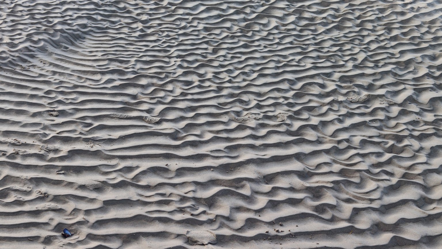 Close-up of rippled sand dunes creating a natural wavy texture in a barren desert landscape.