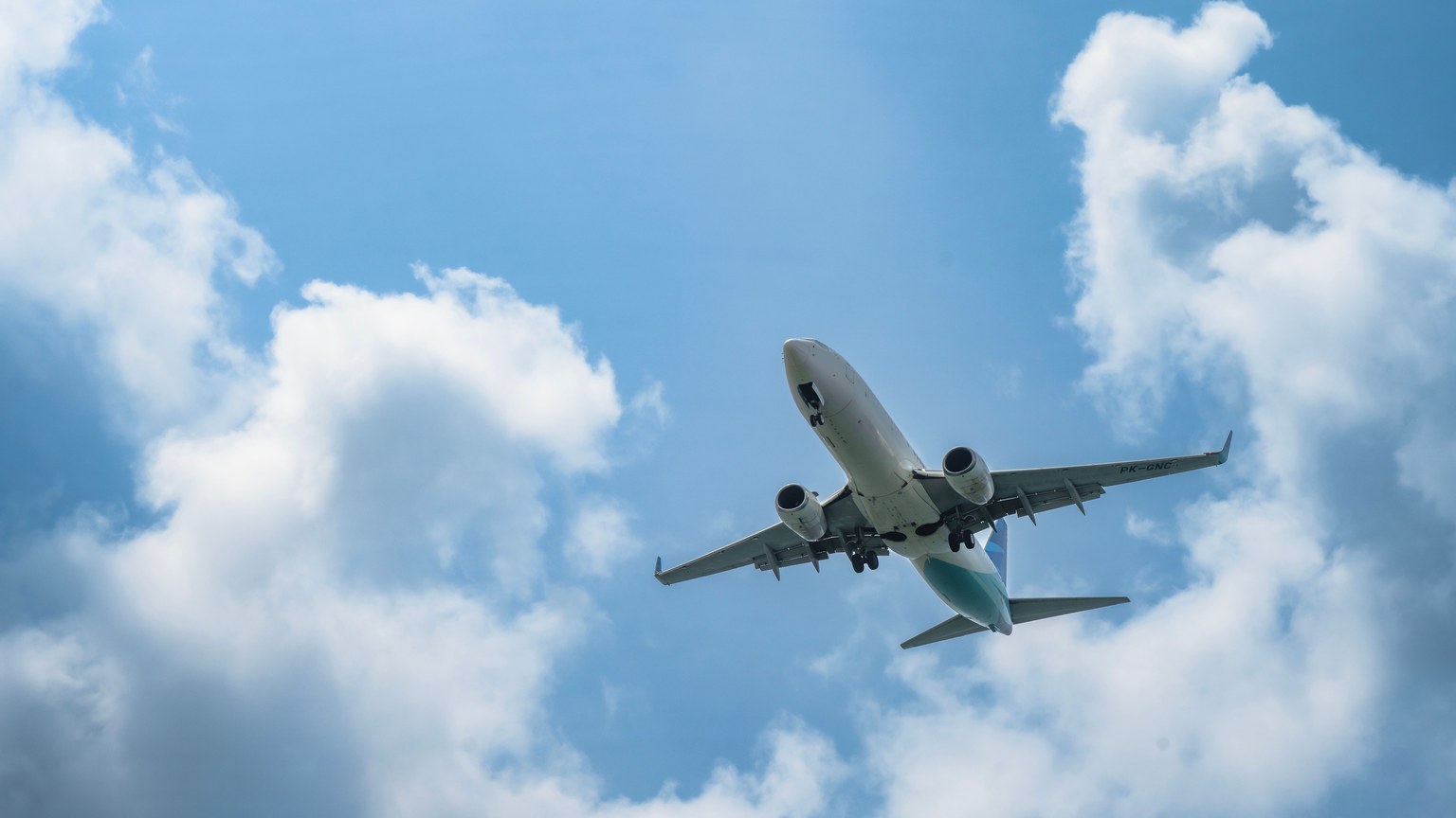A commercial airplane soars in the sky with white clouds and blue backdrop, ideal for travel concepts.