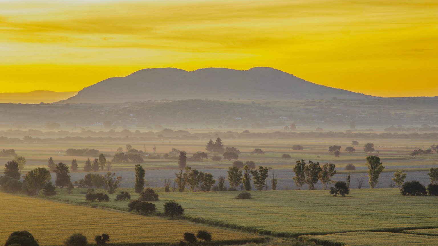 Vibrant sunrise over a tranquil countryside landscape with hills in the background.