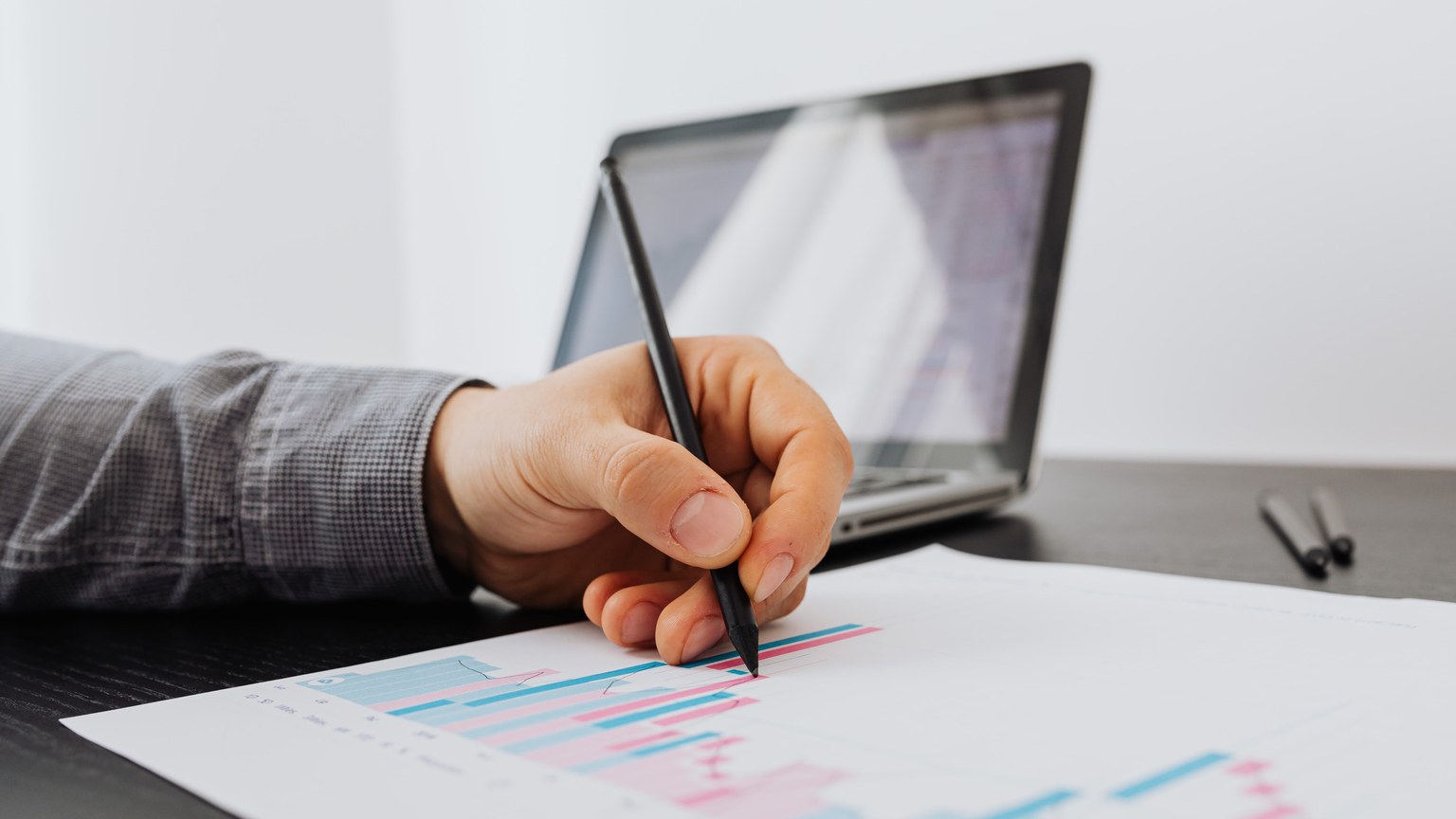 Person taking notes on a business chart with a laptop in the background.