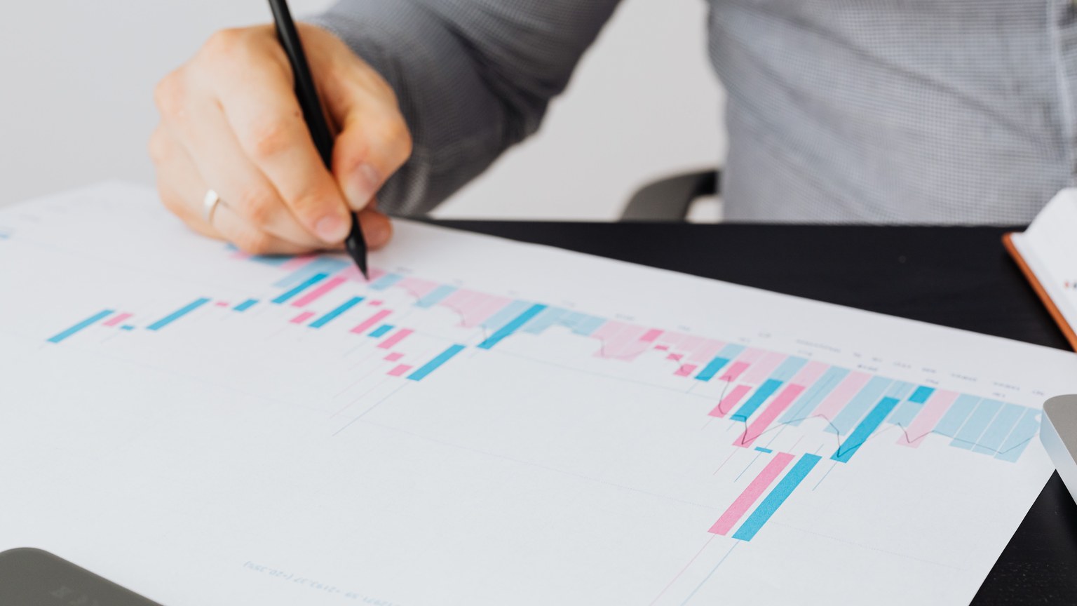 Close-up of a man writing on a printed chart indoors, analyzing colorful data.