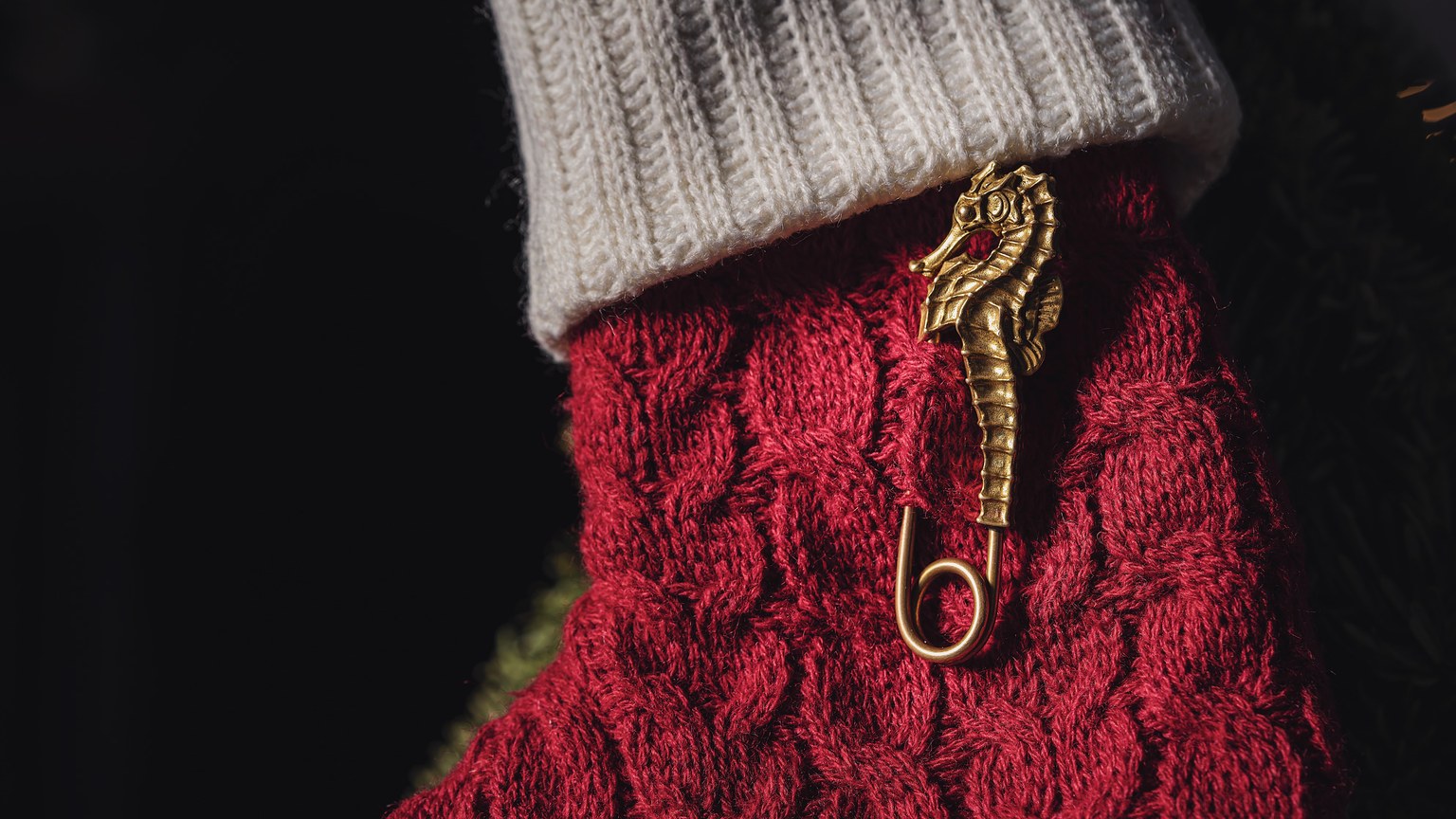 Luxurious golden seahorse pin adorns a red knitted sock, adding charm against a black background.