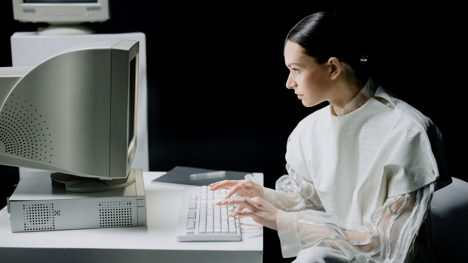 A woman in modern attire using a vintage computer in a dark setting, blending past and future.