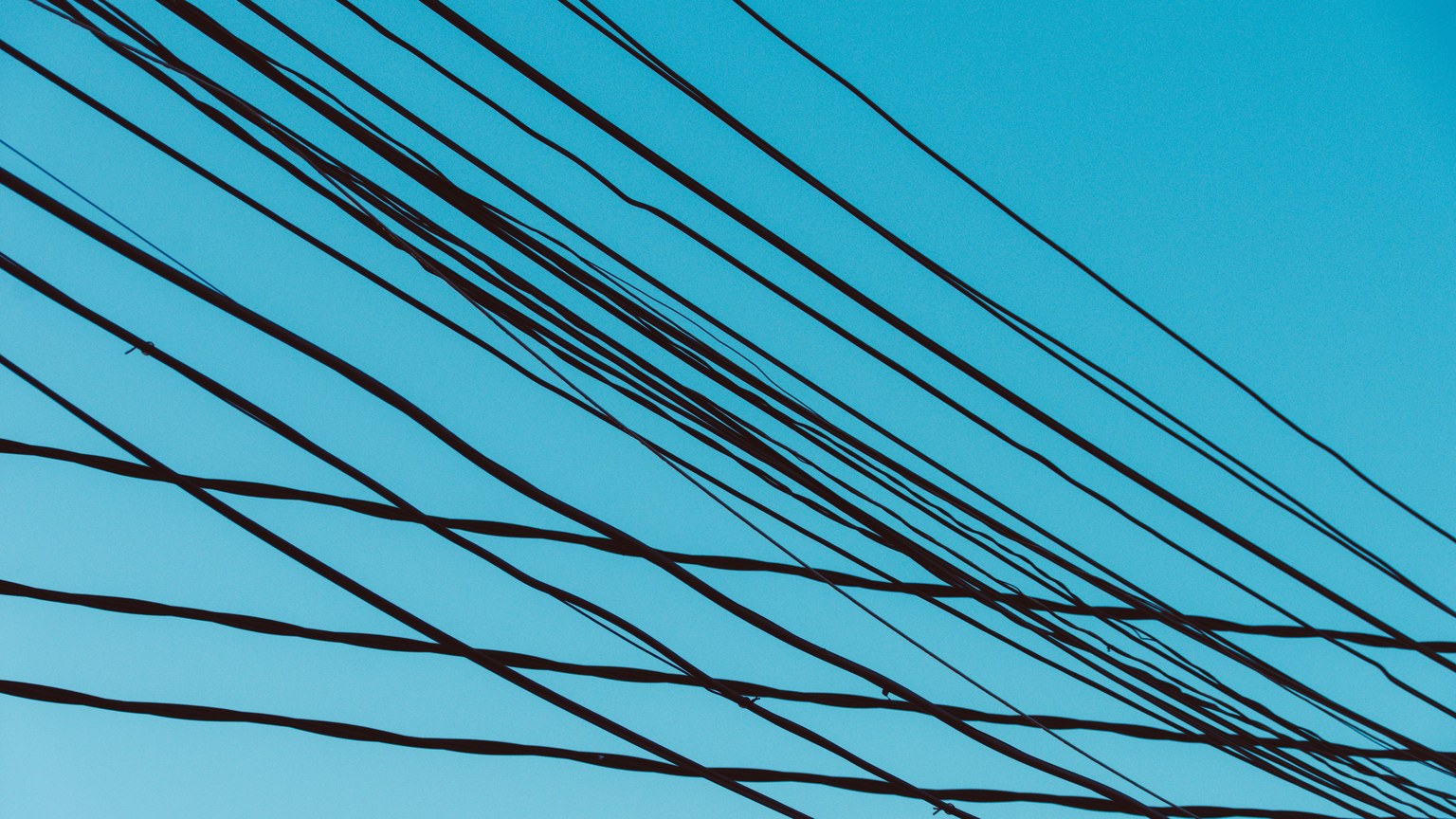 A network of power lines stretched against a vibrant blue sky, creating geometric patterns.