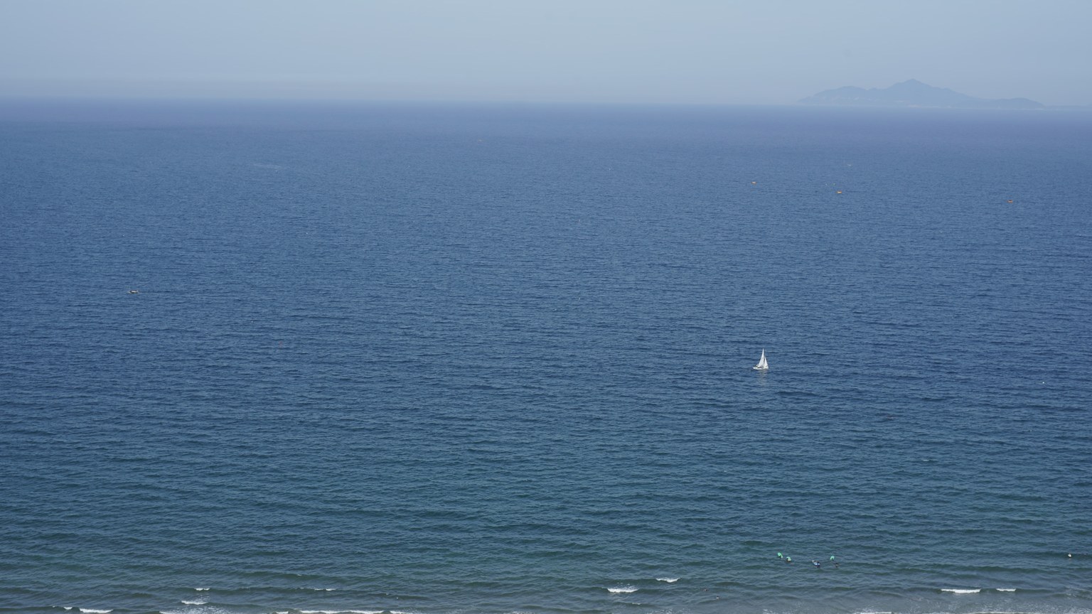 A serene ocean view featuring a distant sailboat on a calm sea under a clear sky.