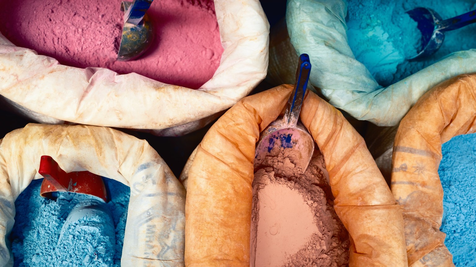 Vibrant colored dye powders in sacks at a market, showcasing traditional craftsmanship.