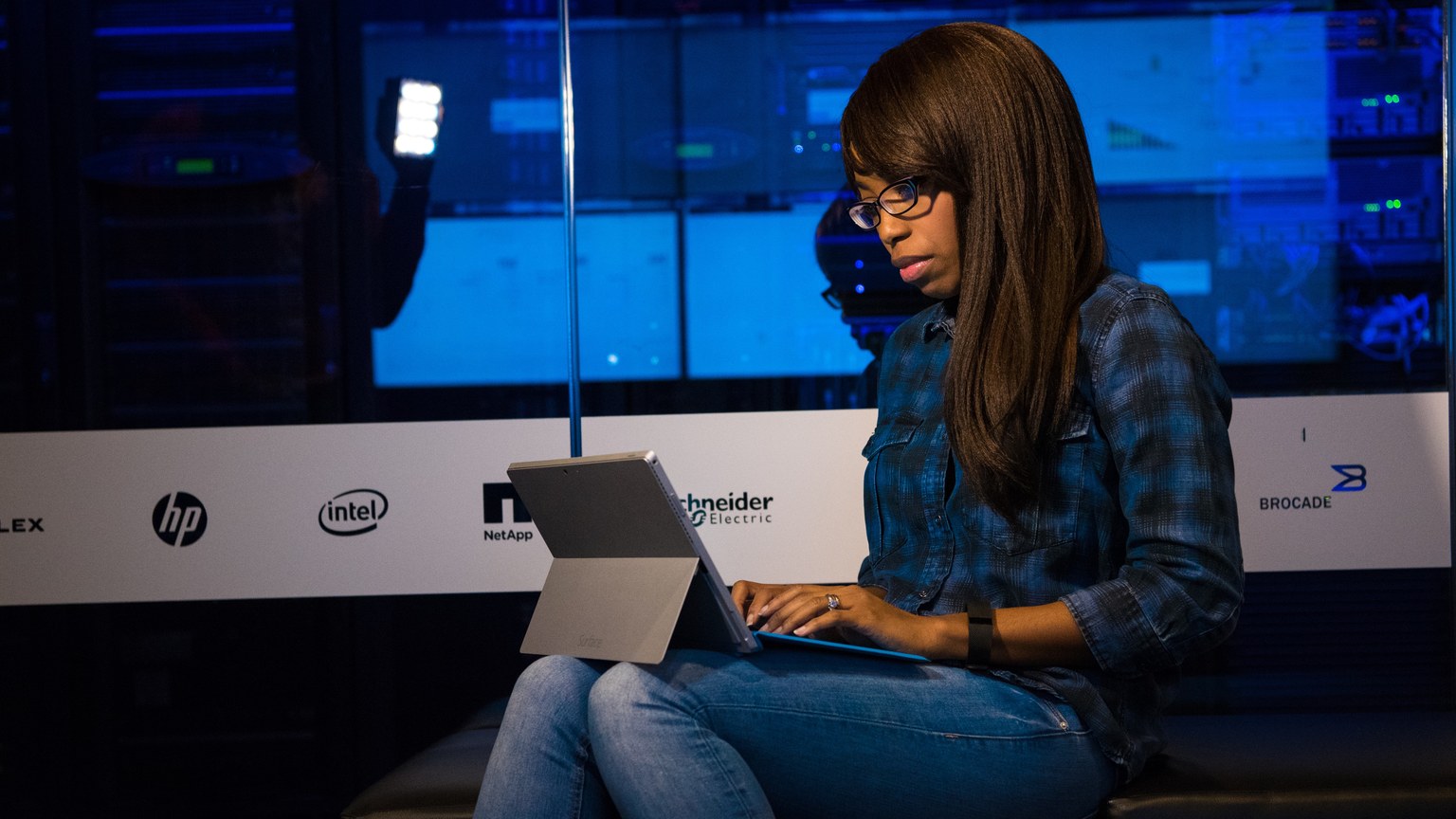 Woman working intently on a laptop in a modern data center environment.