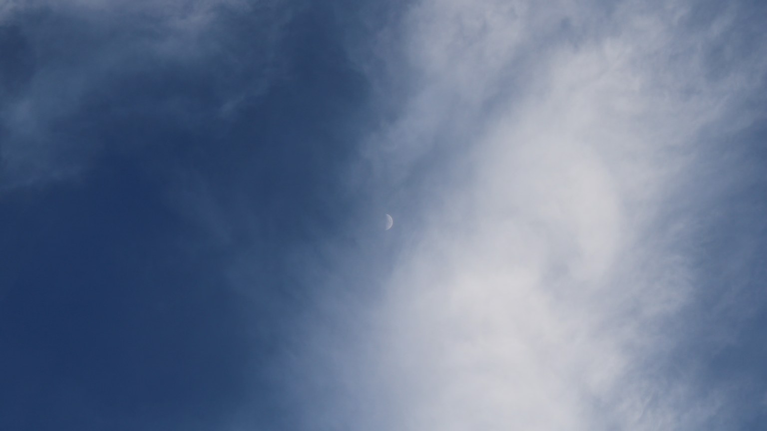 A serene daytime sky with white clouds framing a crescent moon.