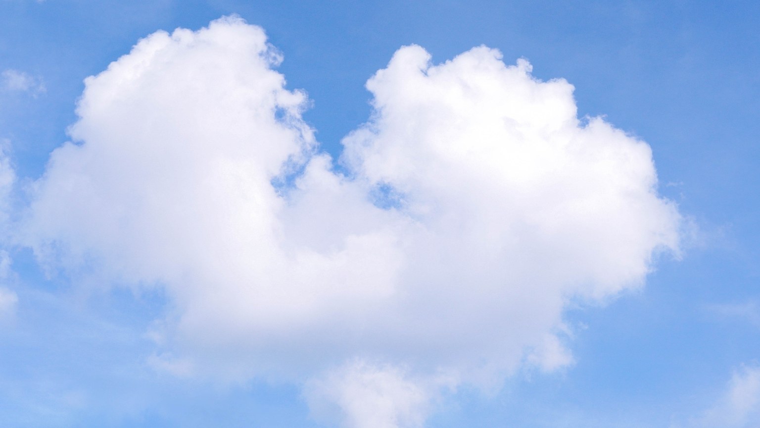 A fluffy, heart-shaped cloud set against a bright blue sky, symbolizing love and nature.
