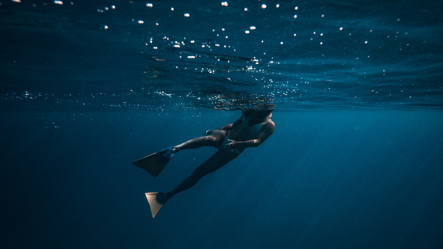 A breathtaking underwater shot of a freediver swimming in deep blue ocean waters.
