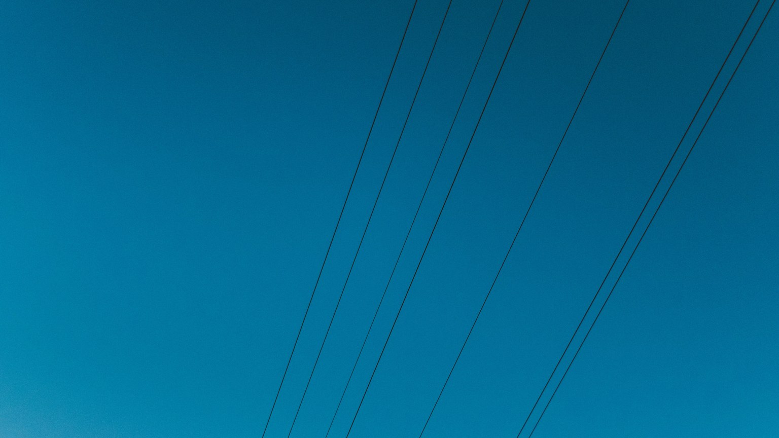 High voltage power lines stretching across a clear deep blue sky.