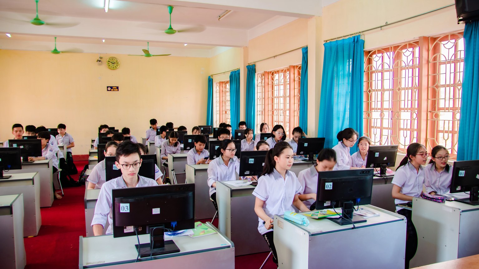 Asian students in uniform learning in a computer lab, focused on their tasks.