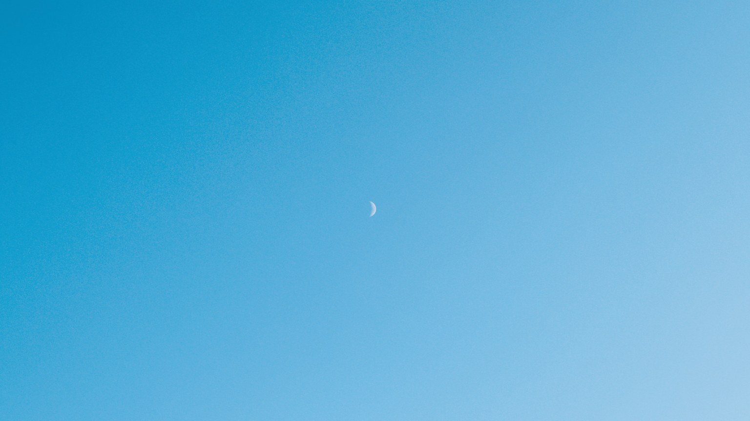 Minimalist image of a crescent moon in a clear blue sky over Samsun, Türkiye.