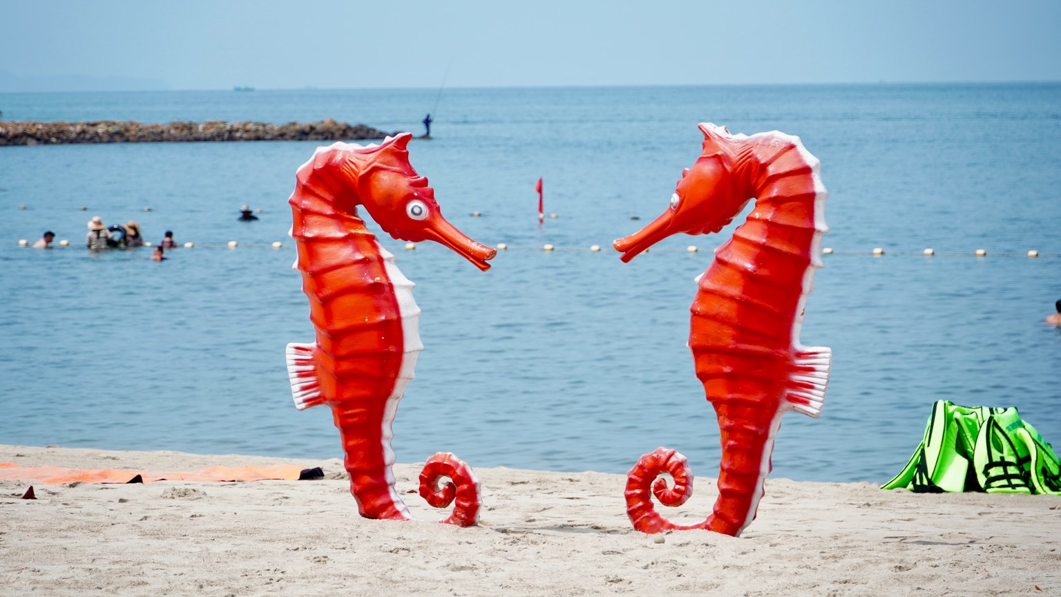 Bright red seahorse sculptures stand on a sandy beach with a calm sea backdrop.