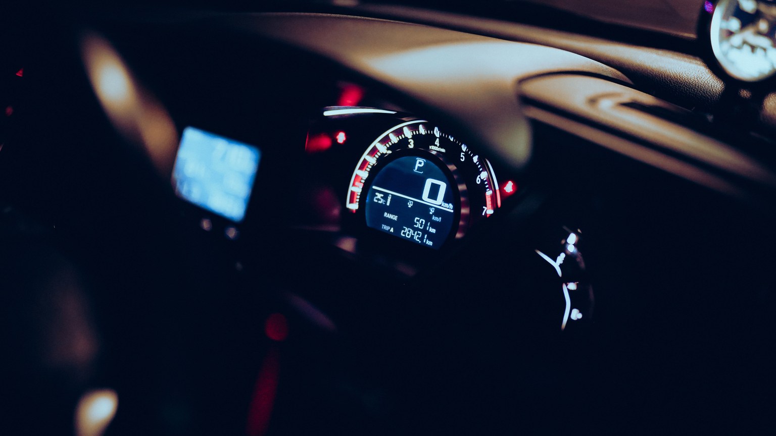 Close-up of a car dashboard at night with illuminated speedometer and tech displays.