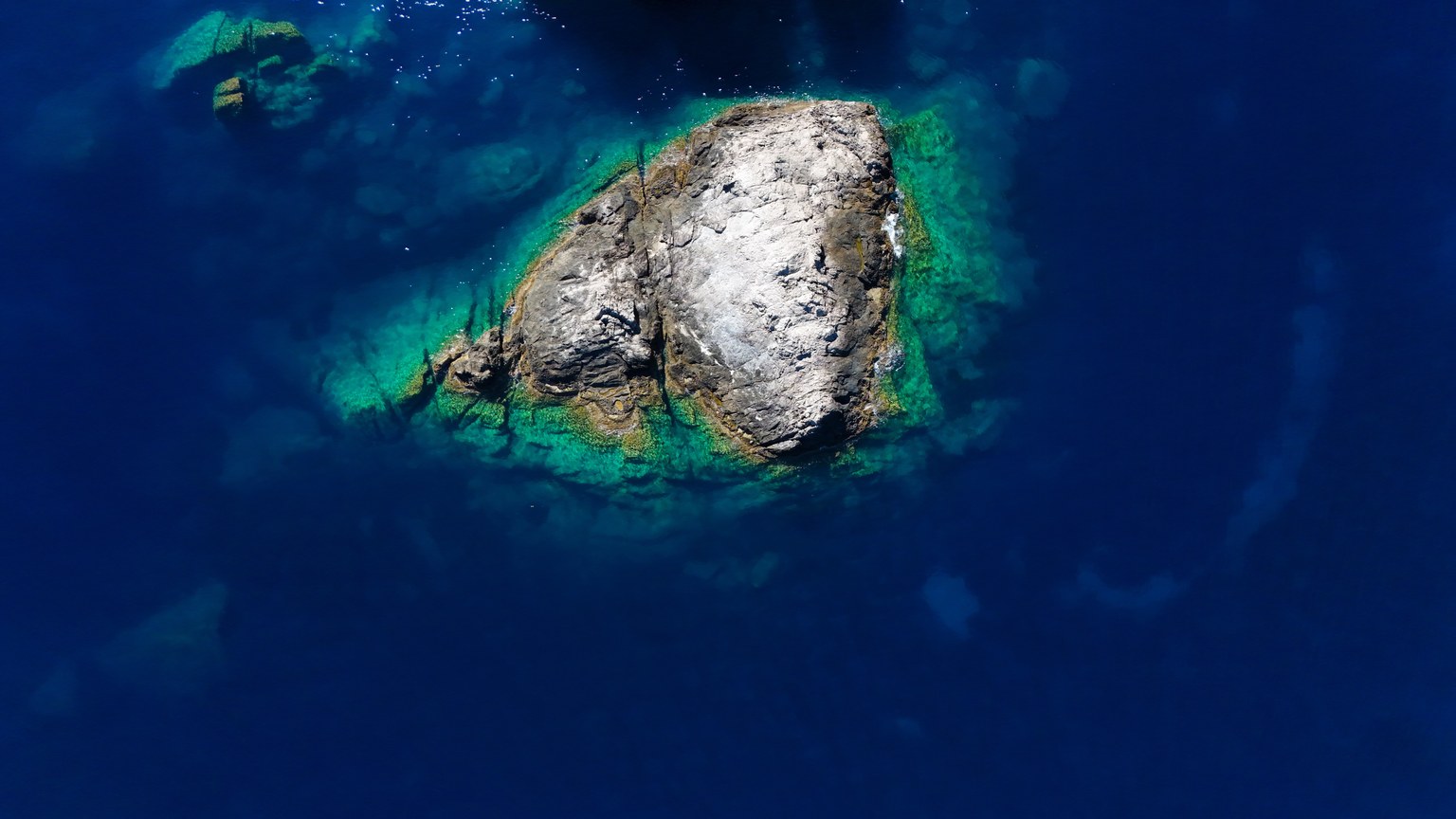 Stunning aerial view of a rocky island surrounded by deep blue waters in Greece.