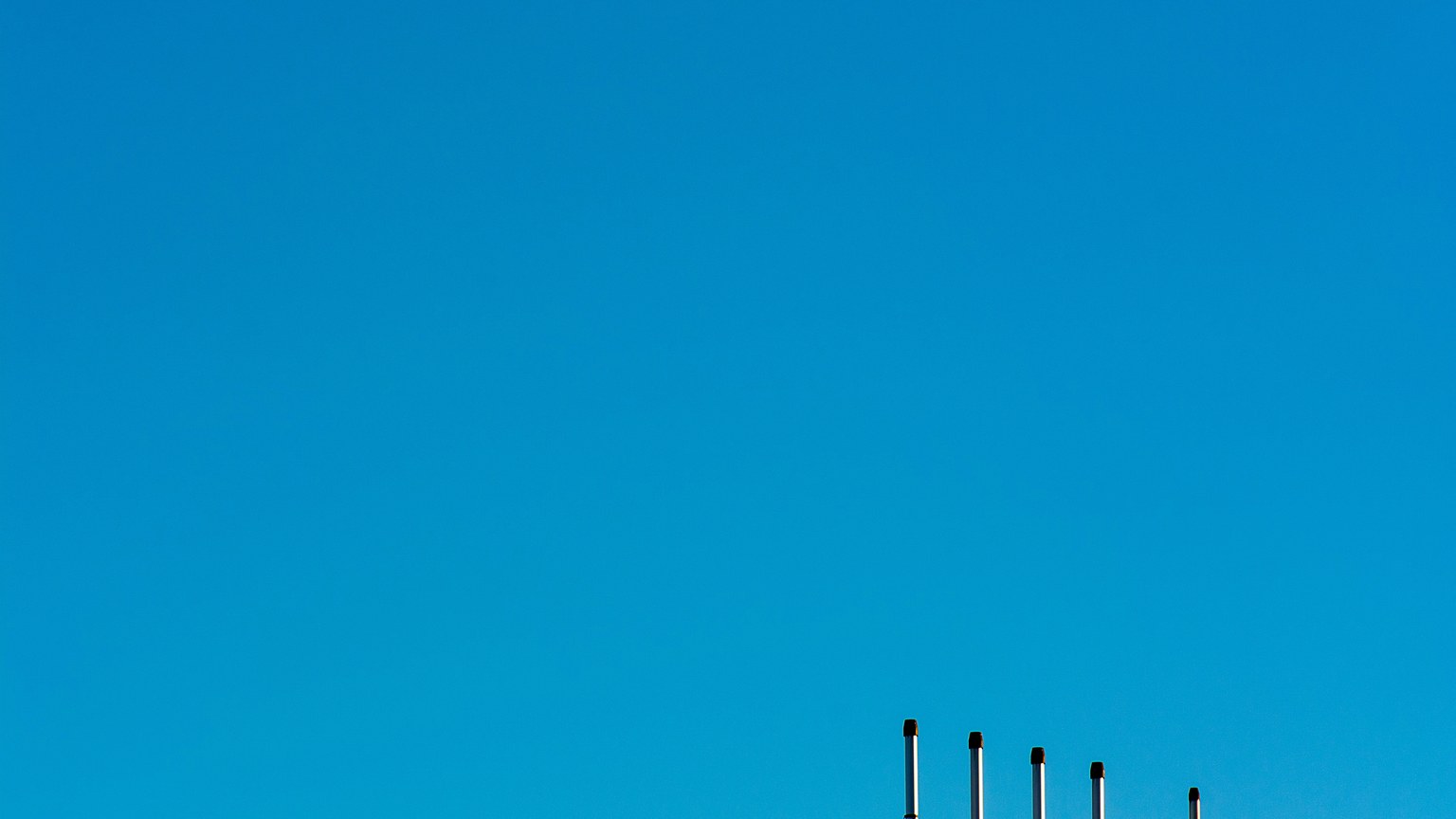 Minimalist image of industrial poles under a clear blue sky, highlighting clean energy.