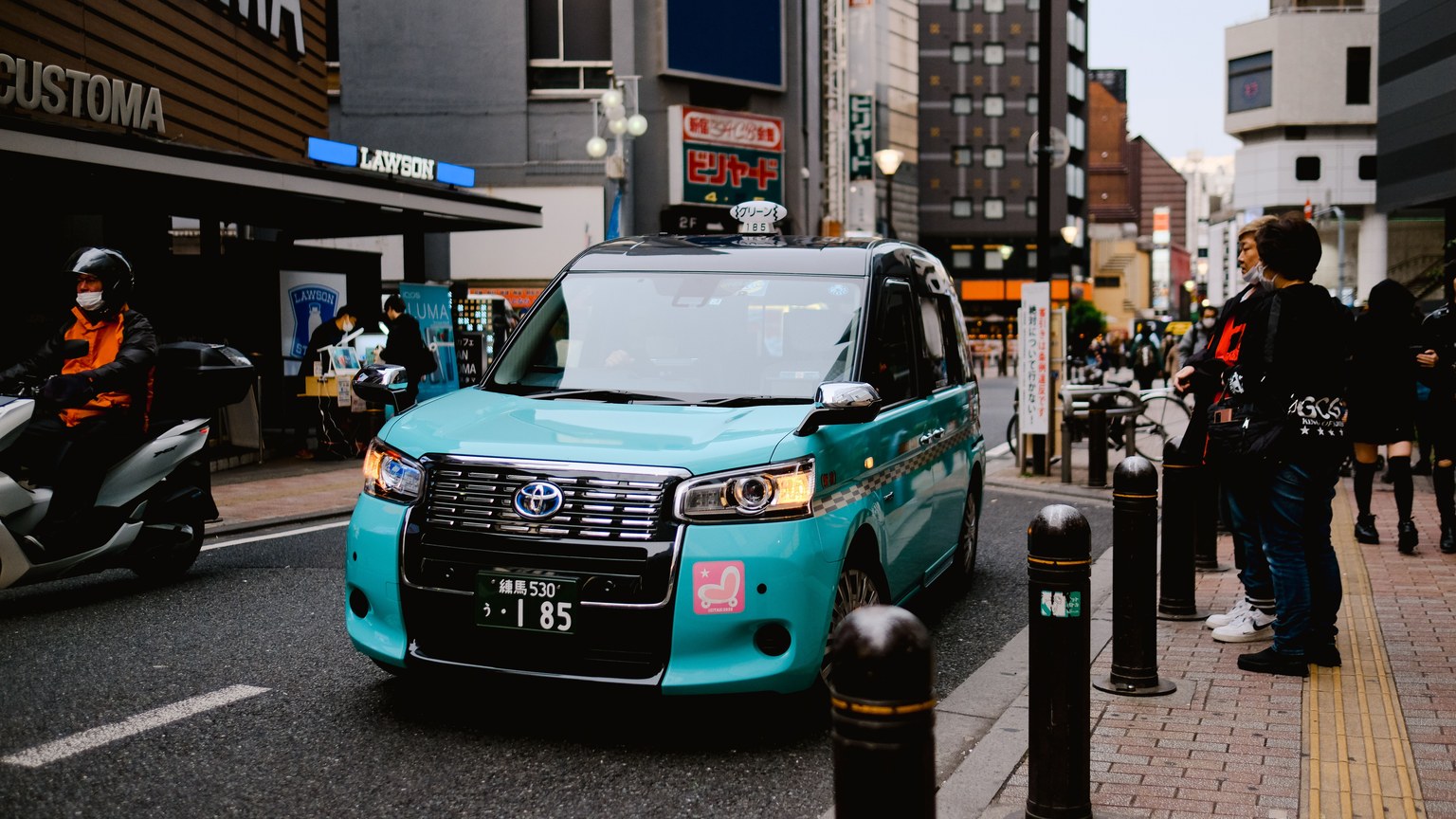 Vibrant urban street in Tokyo featuring a teal taxi, pedestrians, and local shops.