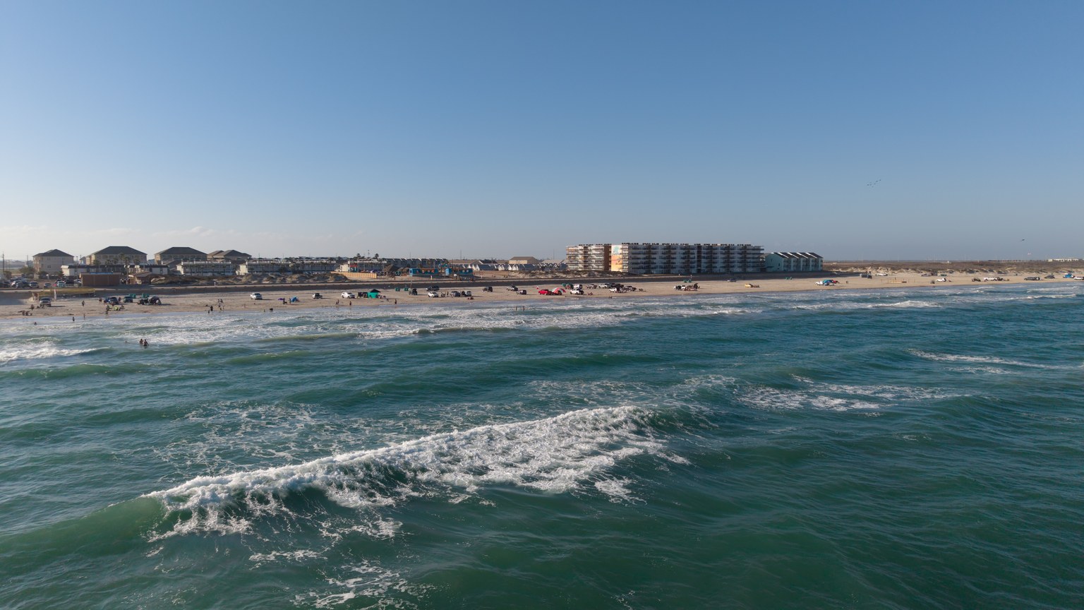 Aerial view of a sunny beach in Corpus Christi with waves and coastal buildings.
