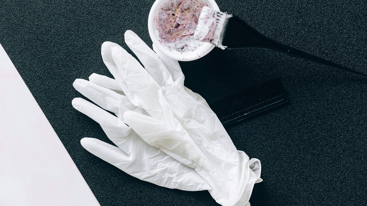 Flat lay of hairdressing tools including dye brush, latex gloves, hair dye bowl, and comb.