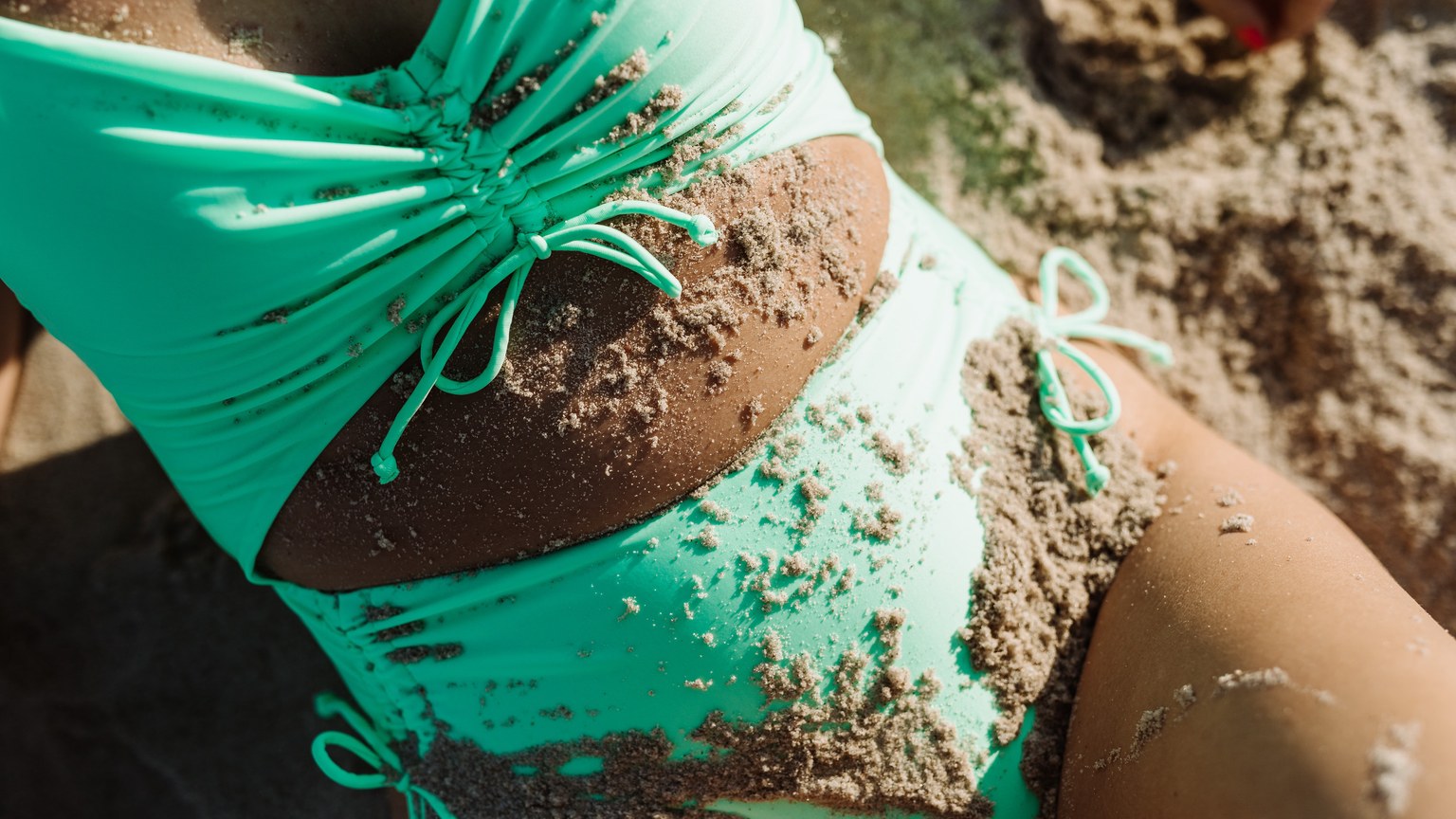 Explore summer relaxation with a teal swimsuit covered in sand on a sunny beach.