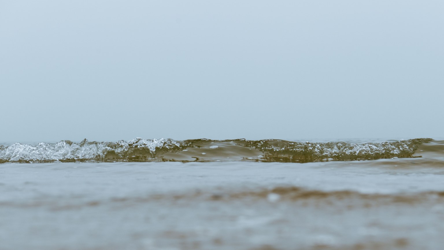 A serene minimalist image featuring gentle waves in an open sea under a misty sky, evoking calmness.