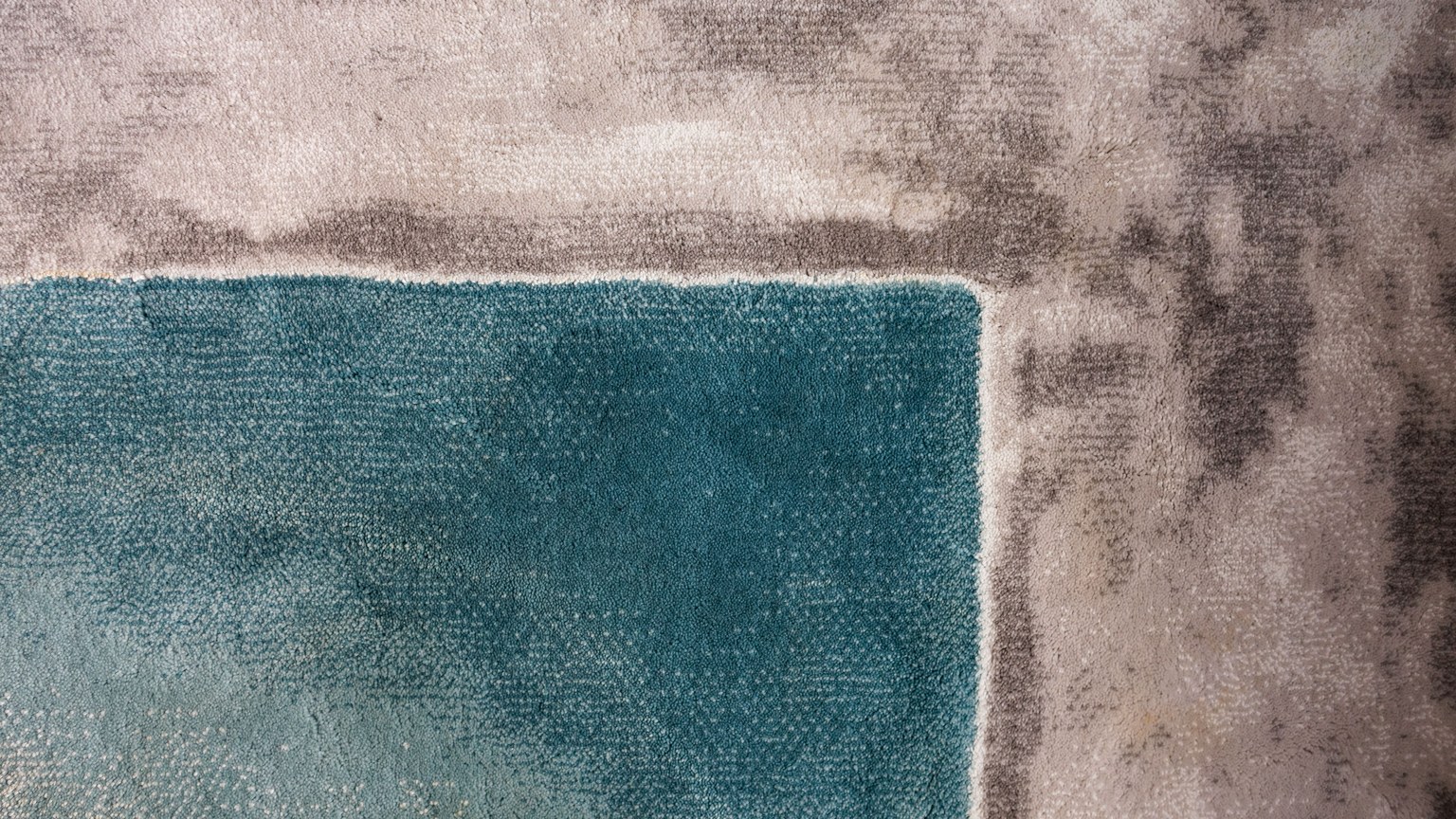 Close-up of a textured carpet showcasing a teal square amidst gray tones.