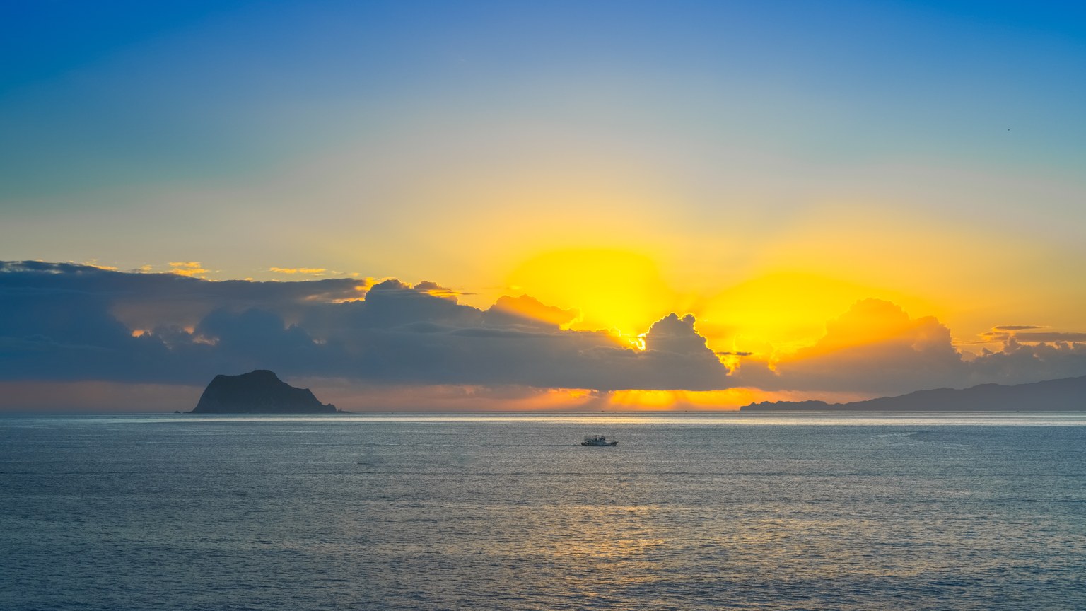 Beautiful sunrise view across the ocean with an island silhouette in the distance.