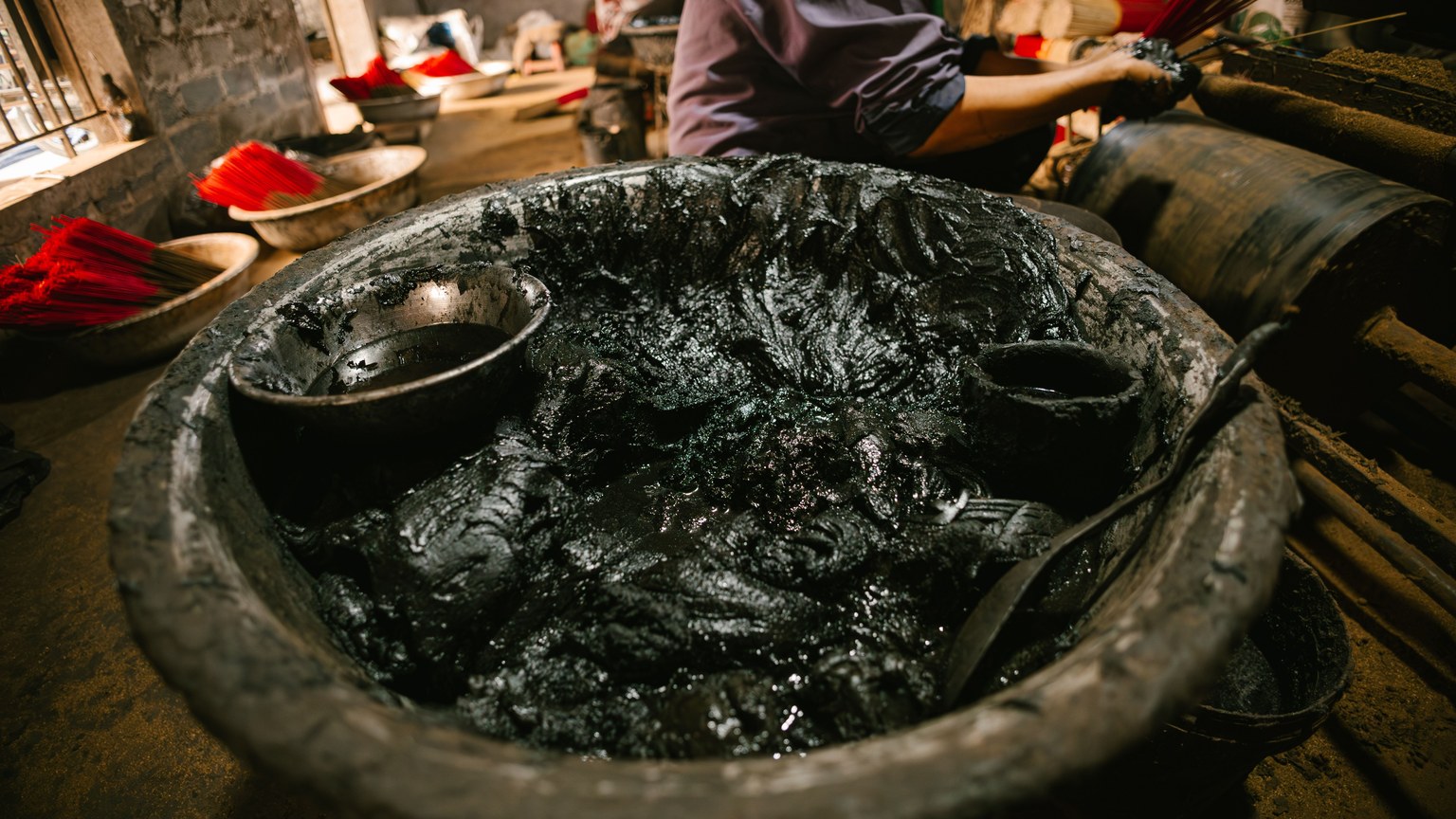 Close-up of a large pot filled with black dye used in traditional incense stick production indoors.