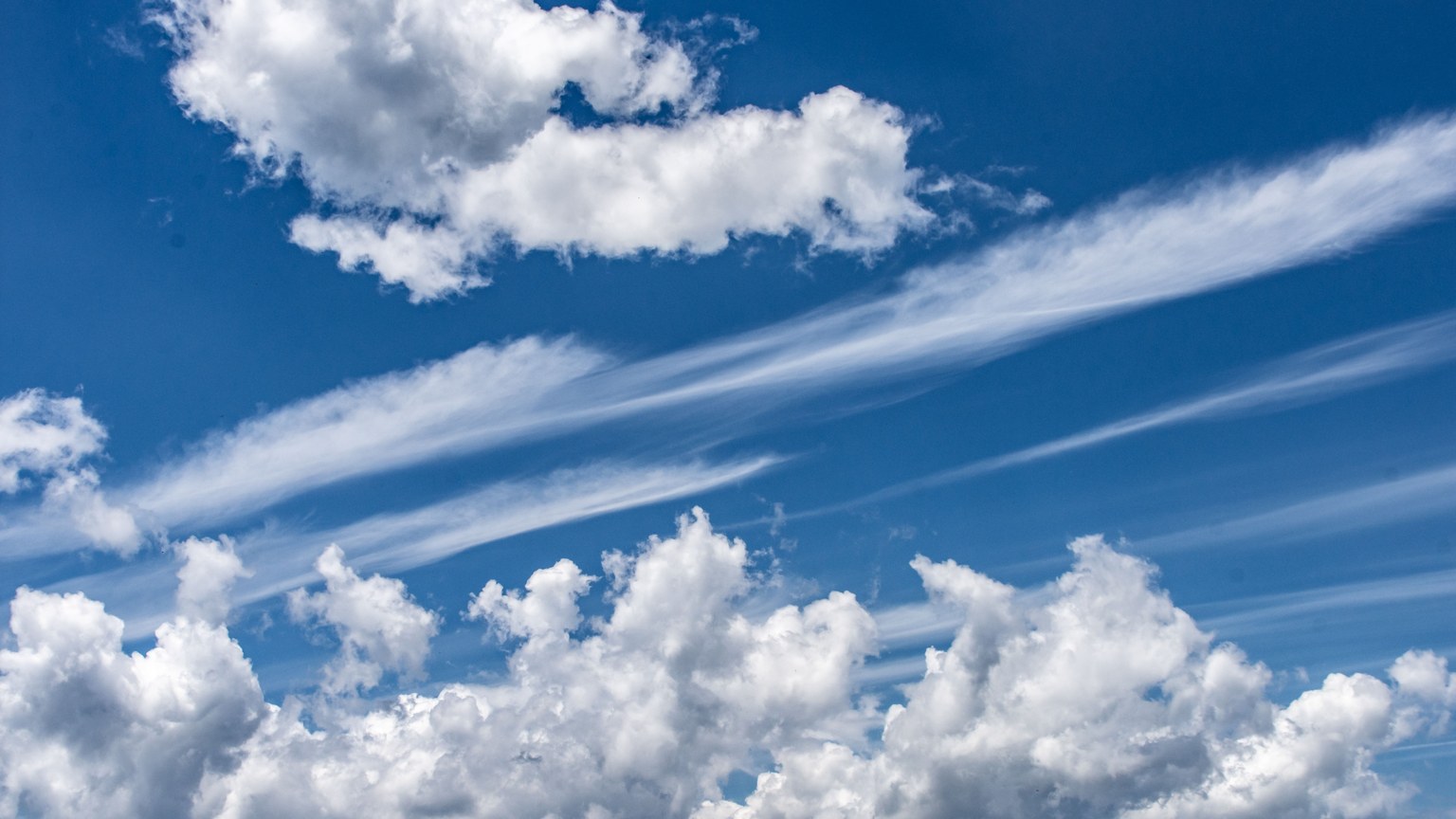 Vivid blue sky filled with fluffy cumulus and cirrus clouds on a sunny day.