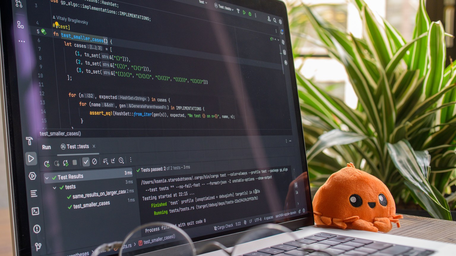 A laptop displaying code in a modern indoor setting with an orange plush toy nearby.