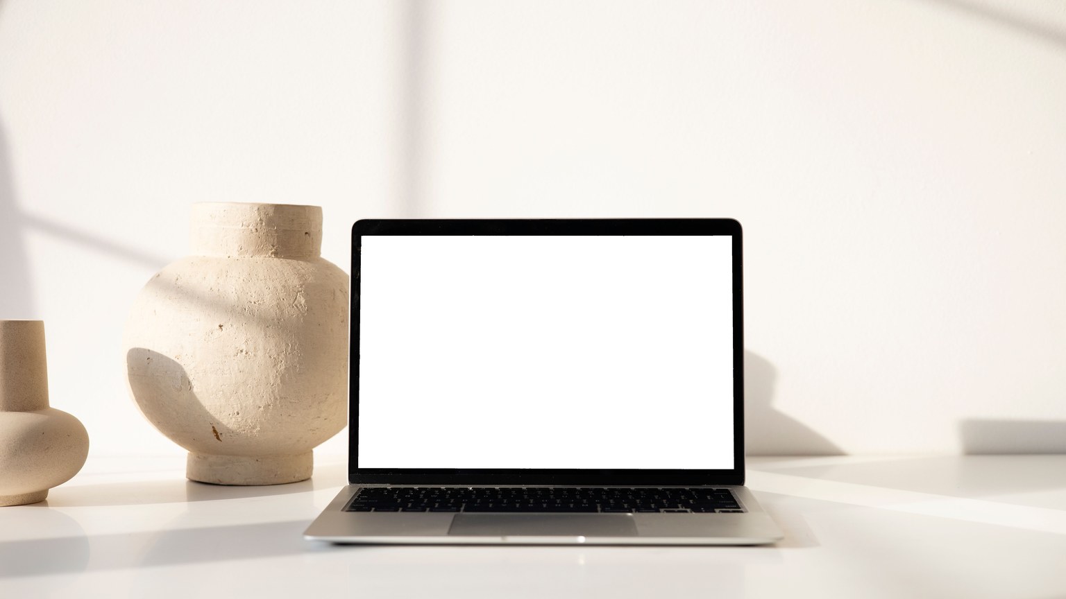Modern minimalist workspace displaying a laptop with clay vases, emphasizing simplicity and style.