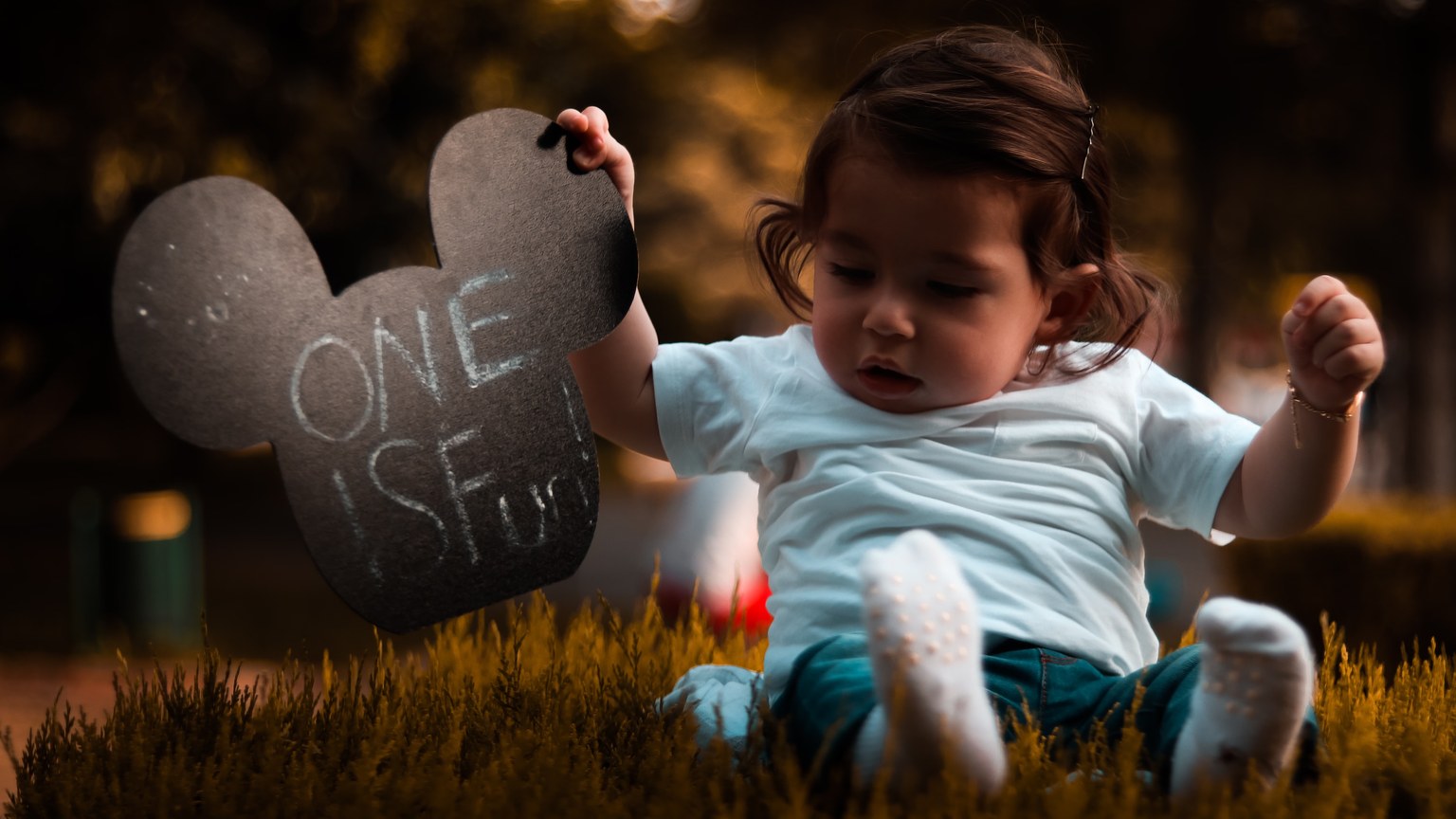 Cute baby playing outdoors holding a Mickey Mouse shaped sign at sunset.
