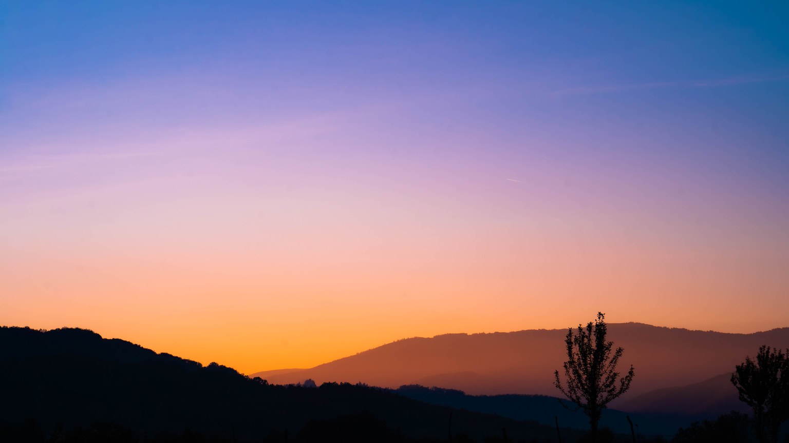 Beautiful silhouette of mountains and trees at sunrise with vibrant sky colors.