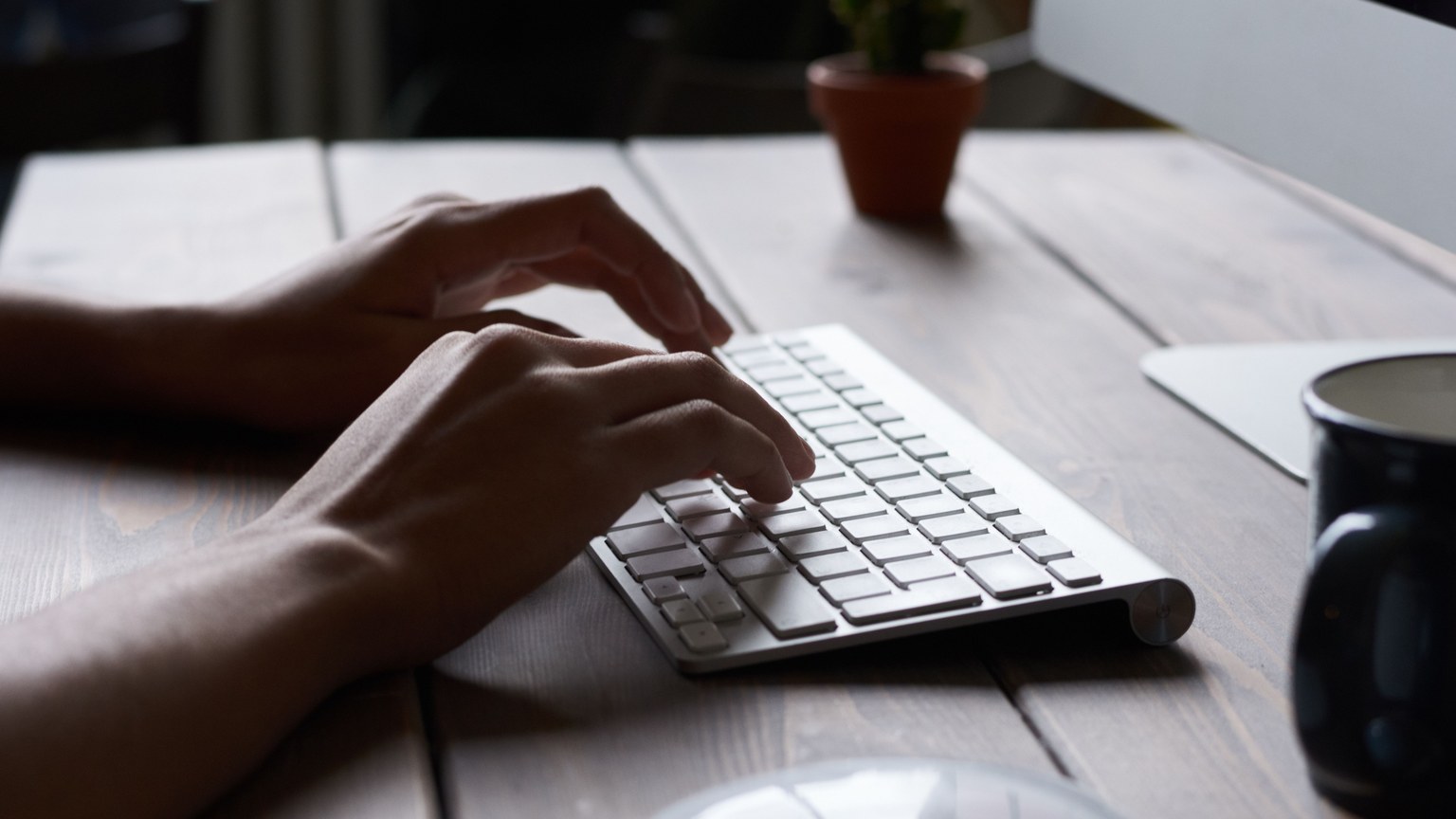Close-up of hands typing on a wireless keyboard at a modern workspace.