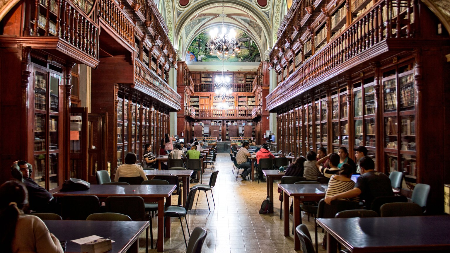 Elegant library with people studying, surrounded by wooden shelves and classical architecture.