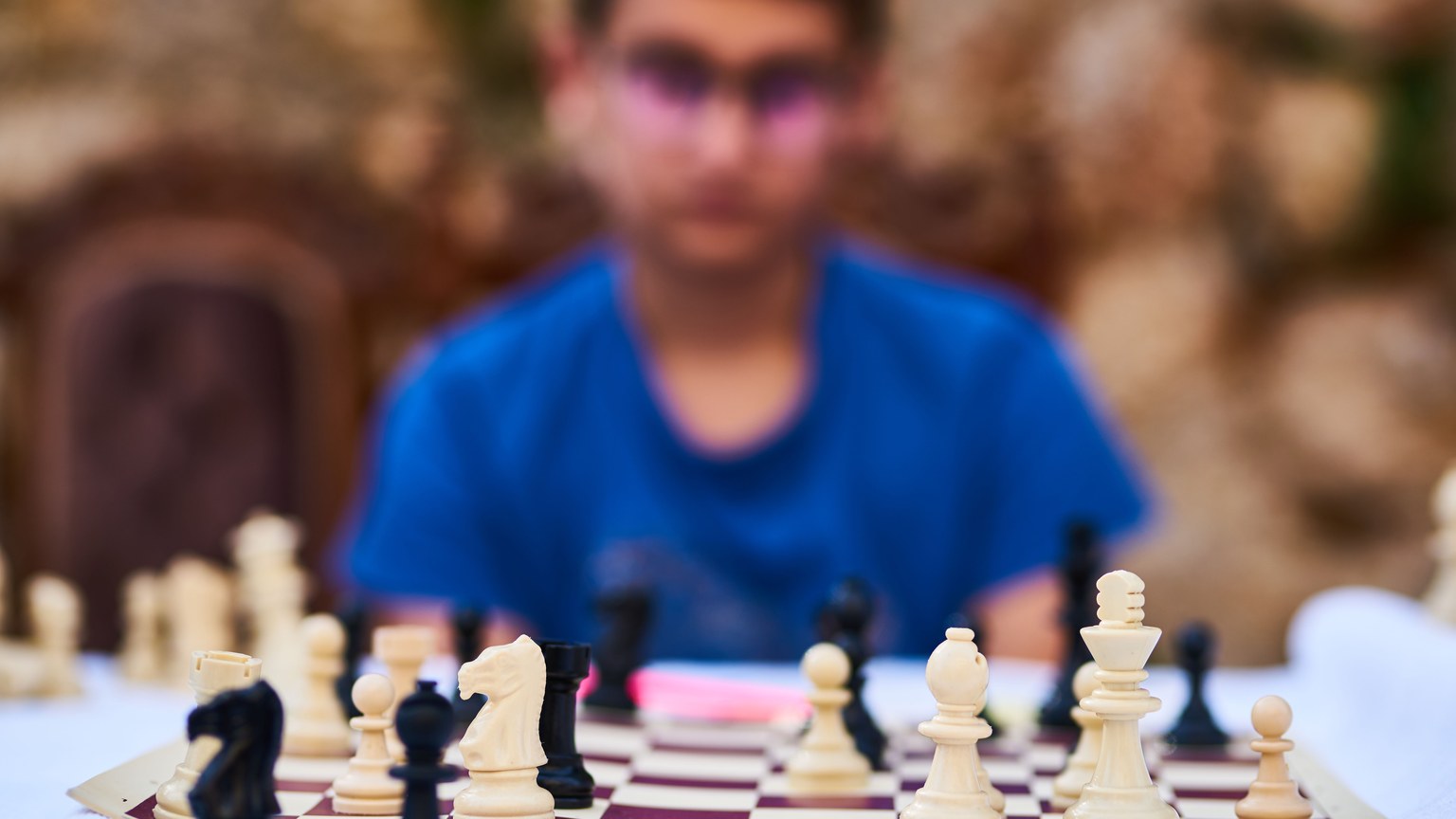 A child focuses on a chess game with blurry background outdoors.