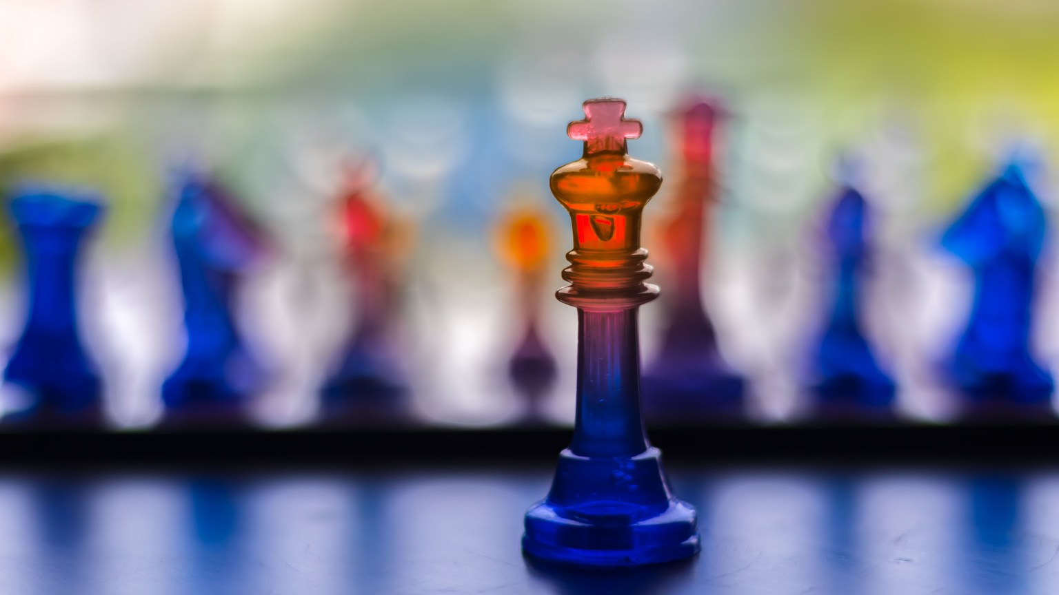 Artistic photo of a vibrant glass chess king with blurred background pieces, showcasing colors and reflections.