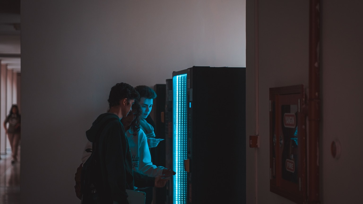 Group of teenagers using a vending machine in a school corridor, captured in ambient lighting.