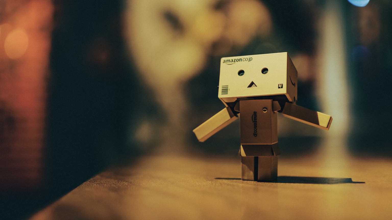 Cardboard toy robot standing on a wooden surface with warm bokeh lights in the background.