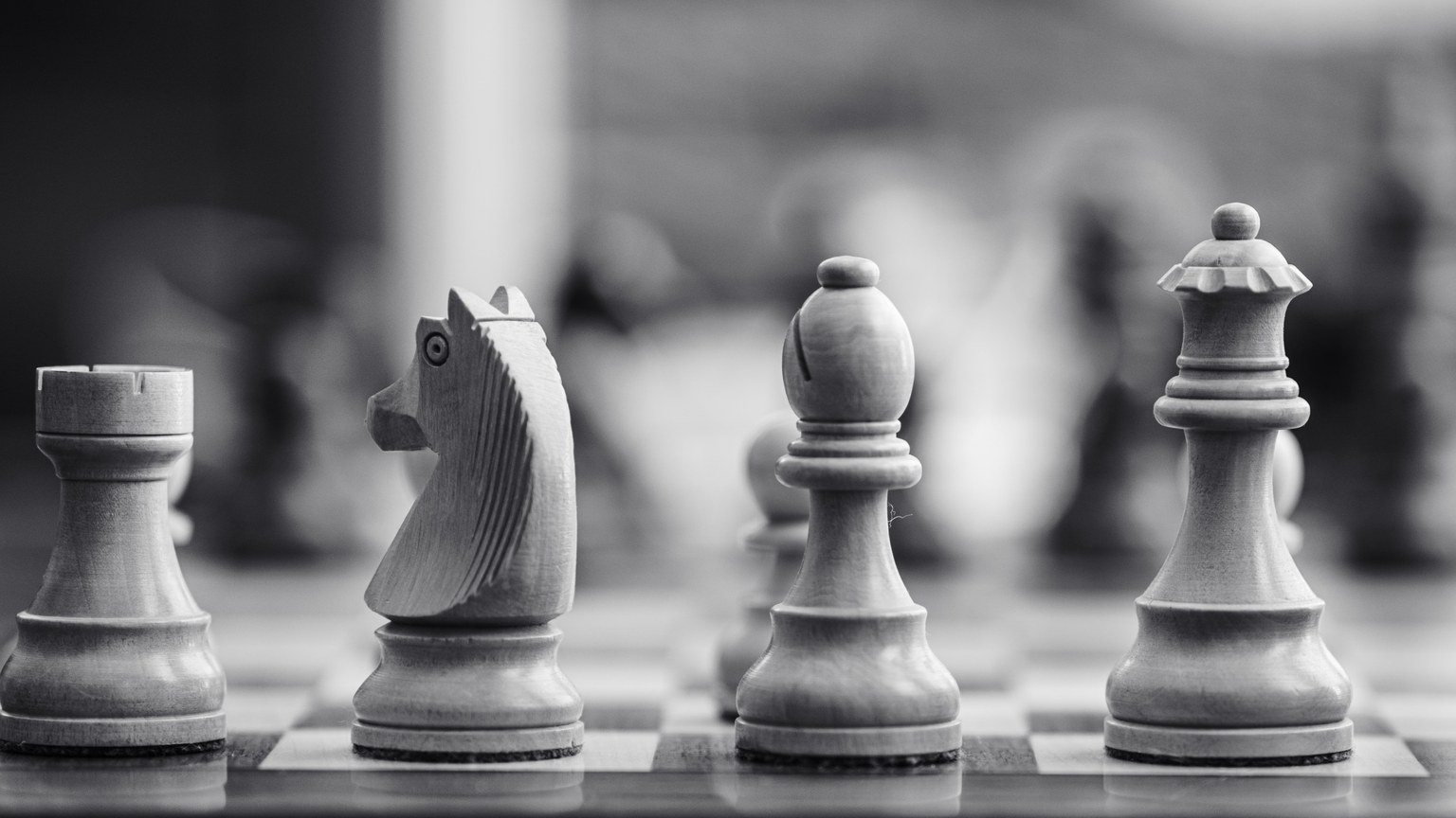 Black and white close-up of wooden chess pieces displayed on a chessboard.