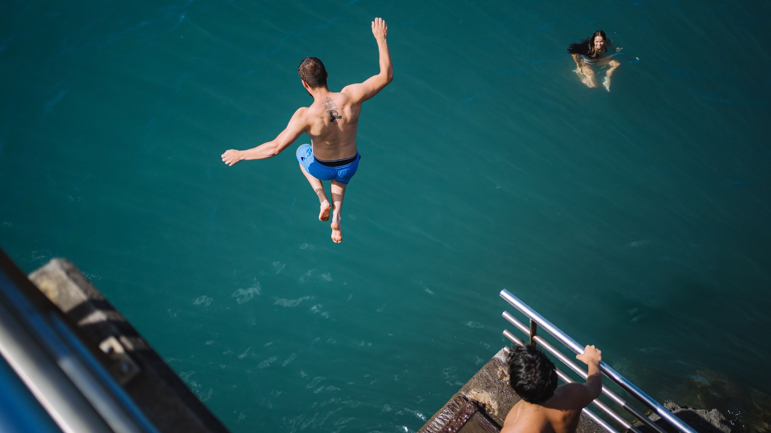 Man diving into the ocean from a ledge with others swimming, showcasing thrilling summer fun.