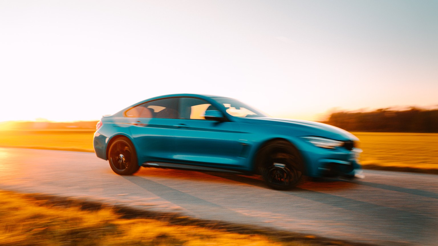 Vibrant blue car speeding on an open road during a serene sunset.
