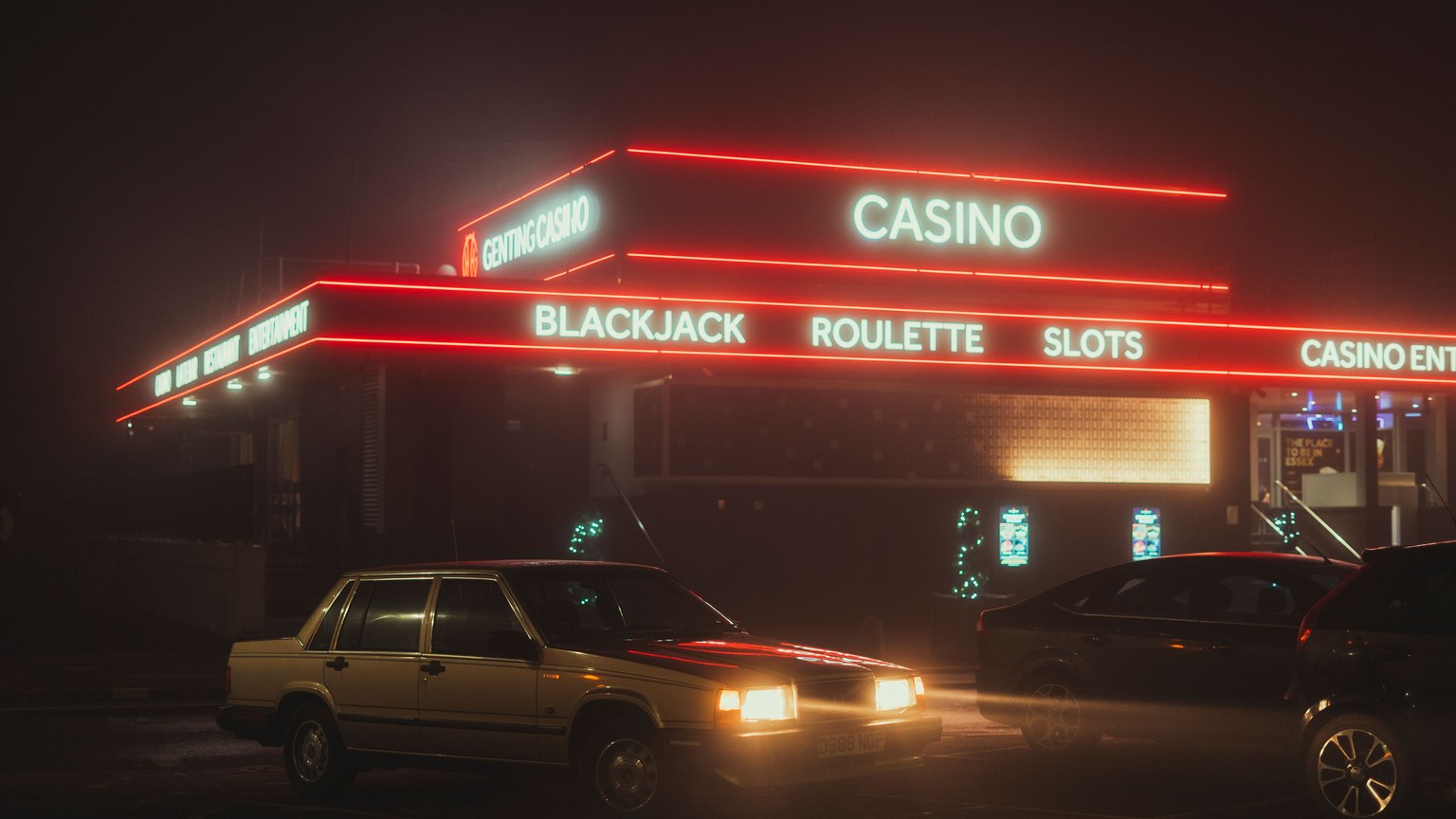 Vintage cars parked outside a neon-lit casino at night, showcasing urban nightlife.