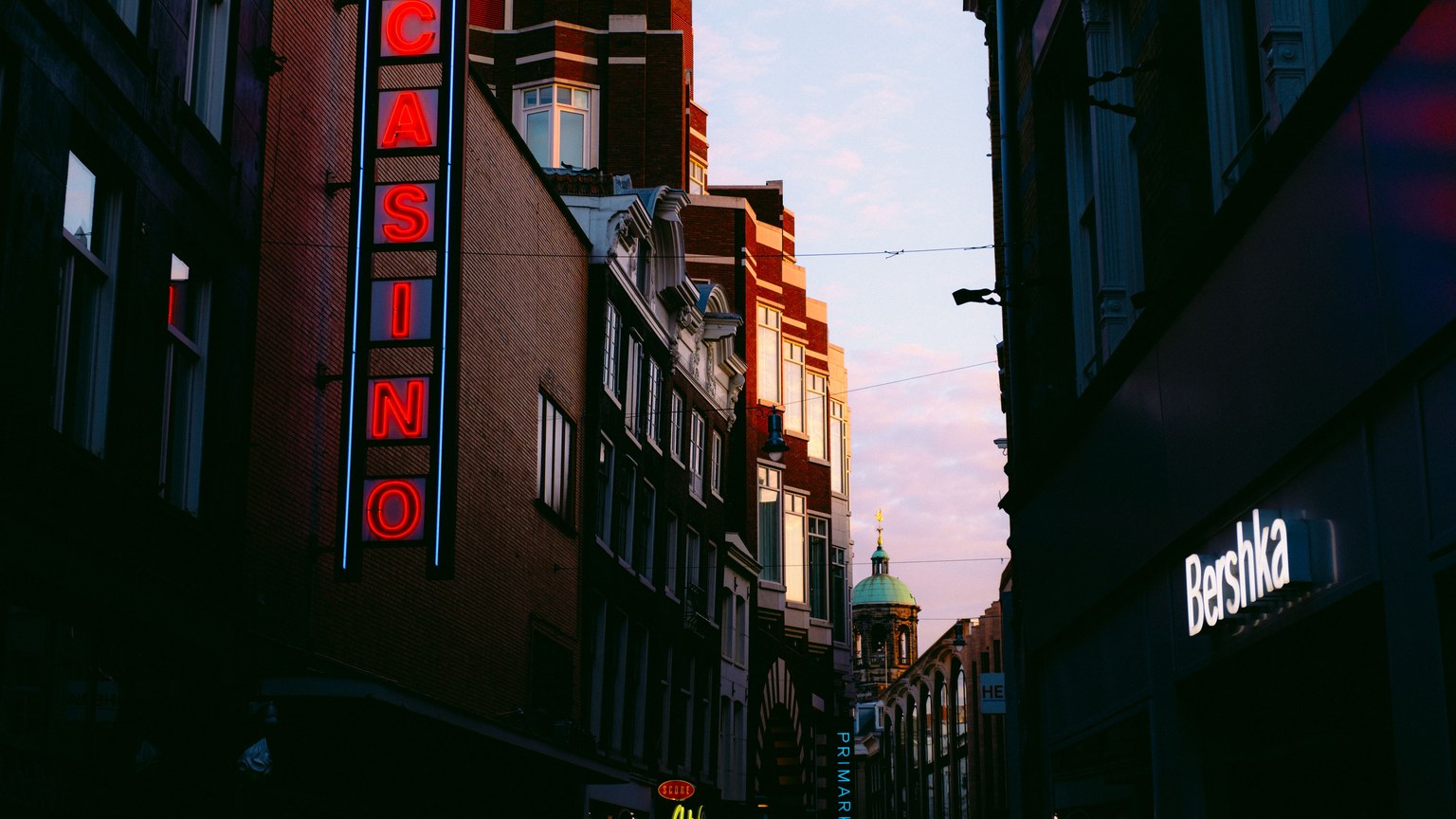 Urban cityscape at dusk featuring neon signs and illuminated streets, creating a lively atmosphere.